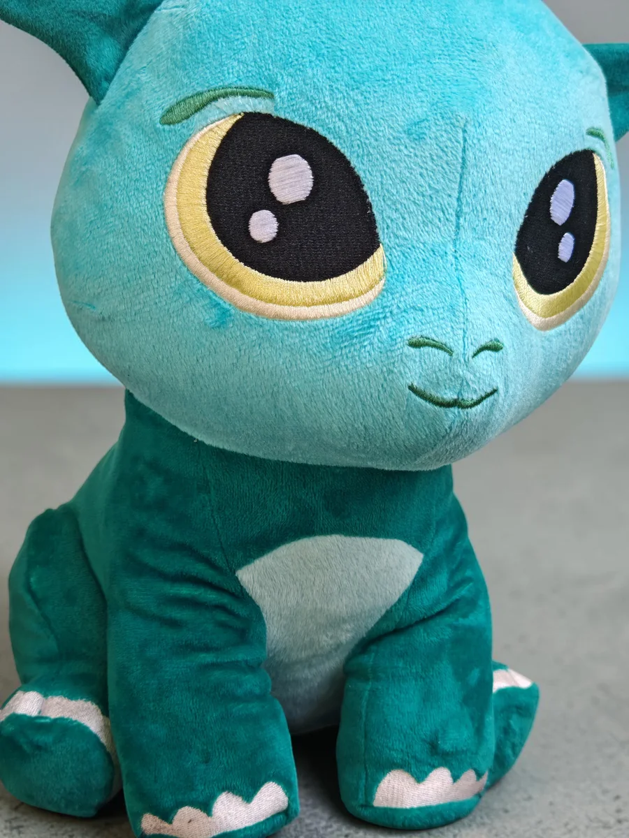 Kobi, the teal-green Playnitive dragon, photographed close up with large embroidered eyes