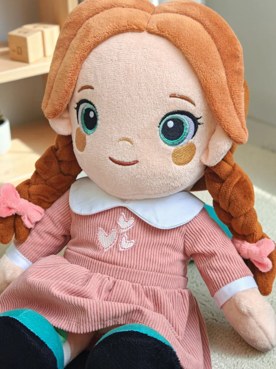 Lotti, the Playnitive doll, photographed close up: auburn braids, embroidered eyes and a pink corduroy dress