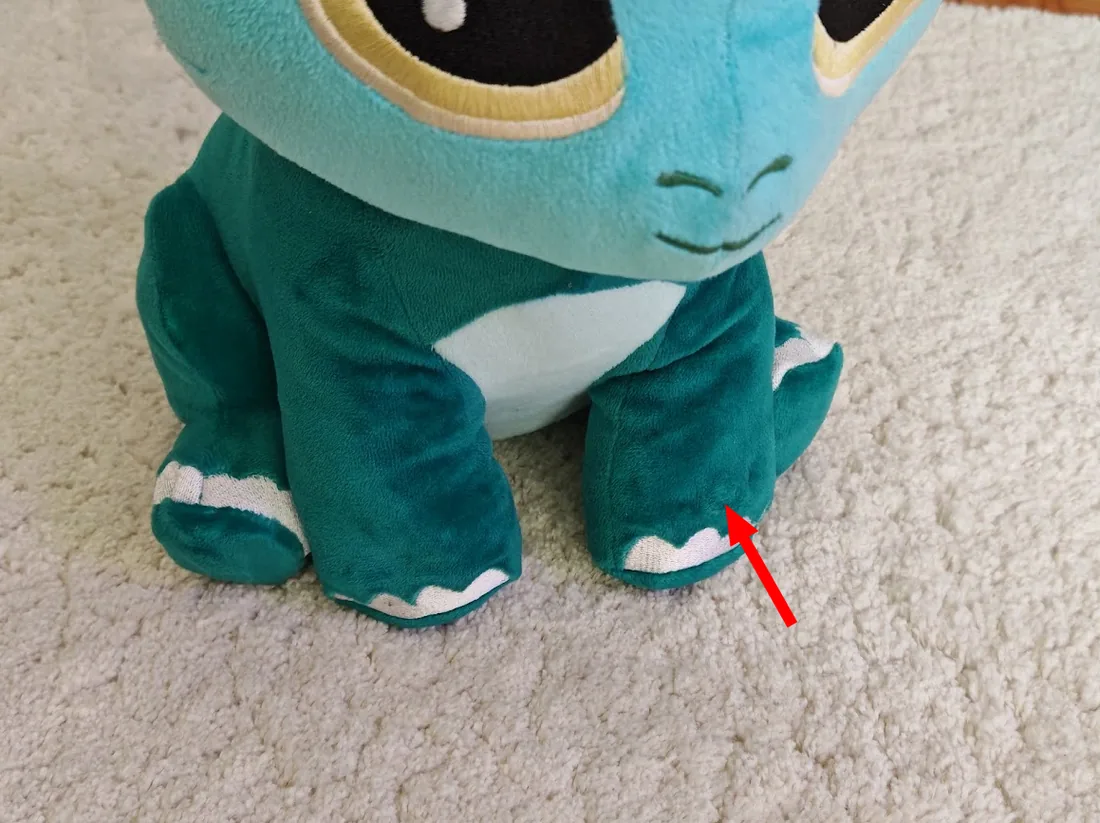 The button in the hand of the plush, marked with an arrow